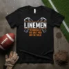 Black t-shirt with white and orange text "LINEMEN TECHNICALLY THE ONLY MEN ON THE FIELD" and football helmet graphics