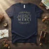 Navy t-shirt with gold "Merci Merci" text in elegant font, surrounded by decorative floral accents