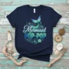 Navy blue t-shirt with "Mermaid POP-POP" text in blue and green gradient, featuring a mermaid tail graphic and nautical elements
