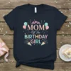 Mom Of The Birthday Girl text with balloons and confetti on a navy blue t-shirt