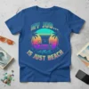Blue t-shirt with "MY JOB... IS JUST BEACH" text, featuring a retro sunset, lifeguard tower, palm trees, and waves graphic