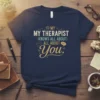Navy blue t-shirt with "My Therapist Knows All About All About You" text in white and gold, featuring a small