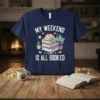 My Weekend Is All Booked text with a cute cat sleeping on books graphic on a navy t-shirt