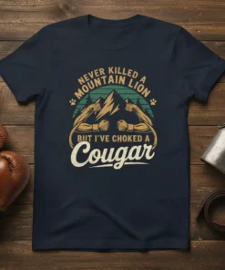 T-shirt design featuring muscular arms, mountains, and the text "Never Killed A Mountain Lion But I've Choked A Cougar"