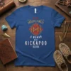 NEVER UNDERESTIMATE A WOMAN WITH KICKAPOO BLOOD text on a blue t-shirt with tribal geometric pattern