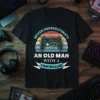 Never Underestimate An Old Man With A Controller T-Shirt featuring a vintage video game controller graphic and retro sunset design