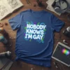 Nobody Knows I'm Gay text in bold white font with neon green and purple accents on a blue t-shirt