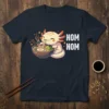 Cute axolotl character eating ramen with "NOM NOM" text, on a navy blue t-shirt