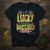 Black t-shirt with "not LUCKY simply BLESSED" text, shamrock pattern, and pink bows, referencing Roman 4:7-8