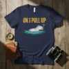 Navy t-shirt with yellow text "OK I PULL UP" above a drawing of a capybara swimming in water with bubbles
