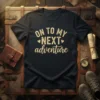 Dark t-shirt with "ON TO MY NEXT adventure" text in a cream vintage font, featuring small heart accents
