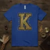 Ornate vintage Letter K monogram design with gold intricate patterns on a royal blue t-shirt