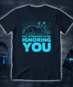 Cyan text "Pay Attention To Me Ignoring You" above a stylized cat illustration on a dark navy t-shirt