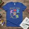 Blue t-shirt with "PEACE AND" text, a red heart, and colorful figures dancing around a golden ribbon and abstract shapes