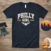 Navy blue t-shirt with "Philly Girl" text in collegiate font and an eagle graphic, representing Philadelphia pride