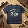 Promoted to G-Pa Est. 2024 text with baby footprints graphic on a navy t-shirt