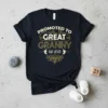 Promoted to Great Granny Est. 2025 text design with baby footprints and floral accent on a black t-shirt