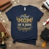 Proud MOM OF A 2025 Graduate text with wings and graduation cap graphic on navy t-shirt