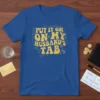 Blue t-shirt with gold retro lettering that reads "PUT IT ON. ON MY HUSBAND'S TAB", surrounded by champagne glasses and