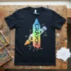 Rainbow CRAYON text on a black t-shirt, with colorful crayon graphics and splatters