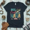 REEL Cool NANA text with a jumping bass fish graphic and floral accents on a navy t-shirt