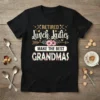 Retired Lunch Ladies Make The Best Grandmas quote on a black t-shirt with floral accents and cutlery graphics