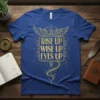 Blue t-shirt with gold text "RISE UP WISE UP EYES UP" in ornate frame, featuring eagle wings and celestial elements