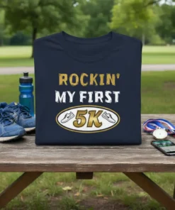 Navy t-shirt with "ROCKIN' MY FIRST 5K" in gold and white lettering, featuring running shoe graphics