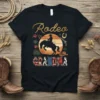 Rodeo Grandma t-shirt with a silhouette of a cowboy riding a horse against a sunset and western-themed graphics