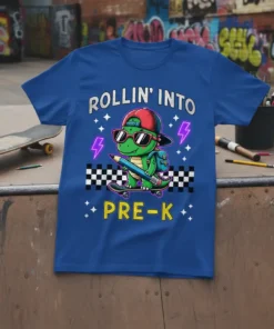 Dinosaur on skateboard with pencil, text "ROLLIN' INTO PRE-K", lightning bolts, and stars on a royal blue t-shirt