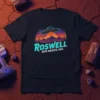 Roswell New Mexico USA t-shirt design featuring a UFO over mountains and cacti, with retro neon text