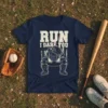 Navy blue t-shirt with "RUN I DARE YOU" text and a baseball catcher graphic, on a distressed American flag background