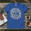 Saved By Grace quote on a blue t-shirt, featuring a floral wreath with birds and elegant gold lettering