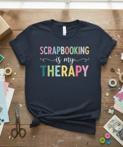 Scrapbooking is my Therapy quote in colorful, playful typography on a navy t-shirt, surrounded by craft supplies