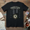 Black t-shirt featuring "SENIOR CITIZEN TEXTING CODE" with lists of humorous texting acronym interpretations and a central shield graphic with