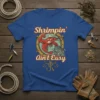 Shrimpin' Ain't Easy T-Shirt with a muscular cartoon shrimp holding a fishing net, nautical theme