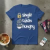 Blue t-shirt with white text reading "single taken hungry" next to icons of a lock, rings, and a bowl of