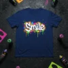 Navy blue t-shirt with "Smile" in white graffiti-style lettering, surrounded by colorful paint splatters and drips