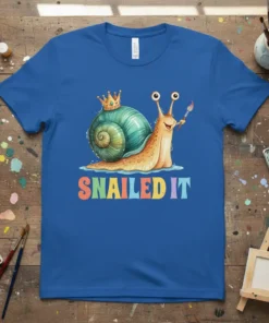 SNAILED IT text with a cute snail wearing a crown and holding a paintbrush on a blue t-shirt