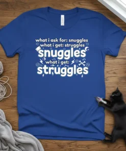 Blue t-shirt with white text: "what i ask for: snuggles, what i get: struggles" repeated, featuring small graphic icons