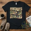 Somebody's Grumpy Ass Husband text design with colorful Christmas lights wrapped around it on a black t-shirt