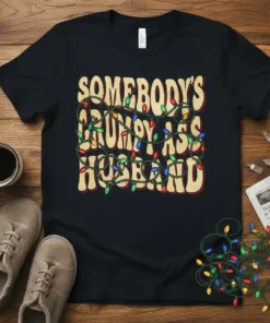 Somebody's Grumpy Ass Husband text design with colorful Christmas lights wrapped around it on a black t-shirt