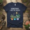 Navy t-shirt with white text "Sometimes I Wet My Plants" above a watercolor illustration of three potted plants being watered