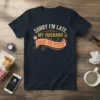 Funny "Sorry I'm Late My Husband Had To Poop" quote t-shirt design in yellow and orange text on a navy