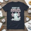 Cute axolotl graphic with text "Sorry My Axolotl Ate My Homework" on a navy t-shirt