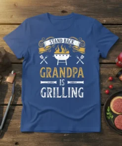 Stand Back Grandpa Is Grilling text design with barbecue grill graphic and utensils, on a blue t-shirt