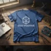 Blue t-shirt with white text 'STAY POSITIVE' and a geometric outline design above it