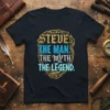 Steve The Man The Myth The Legend quote on a black t-shirt with gold and blue typography, framed by ornate