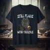 Black t-shirt with white text "STILL PLAYS WITH TRUCKS" above a detailed engine graphic, a wrench, and a sunset truck