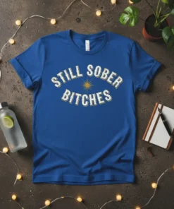 Blue t-shirt with distressed white text "STILL SOBER BITCHES" and a yellow sunburst graphic